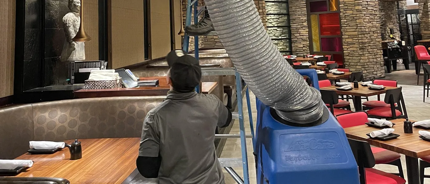 Technician using negative-pressure air duct cleaning machine and hose to clean commercial ductwork in Las Vegas